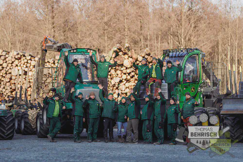 Teamfoto Forstbetrieb Thomas Behrisch – alle Mitarbeiter in grüner Arbeitskleidung vor Forstmaschinen und Holzpolter