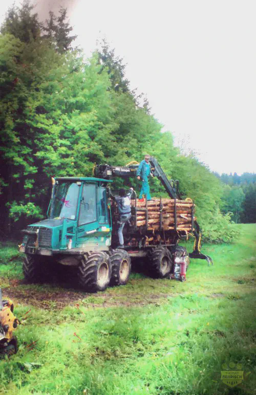 Timberjack-Forwarder wird von Mitarbeiter mit Rundholz beladen am Waldrand