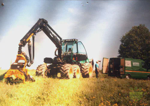 Großer Harvester mit Fällkopf neben einem Forst-Servicefahrzeug auf einer Wiese