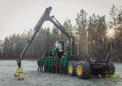 Das gesamte Team des Forstbetriebs Behrisch vor einem großen Forwarder im Morgenlicht