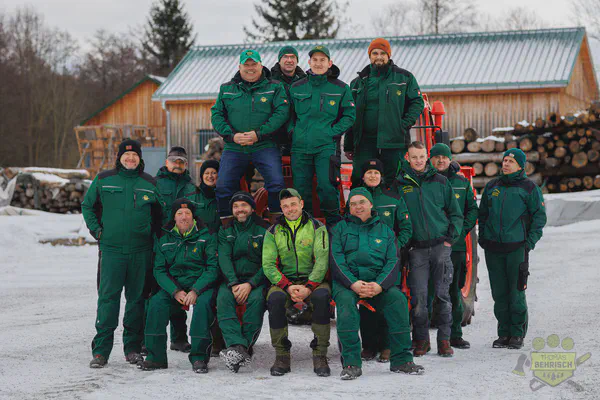 Gruppenfoto des Behrisch-Teams in drei Reihen vor einem roten Forsttraktor auf dem Betriebshof