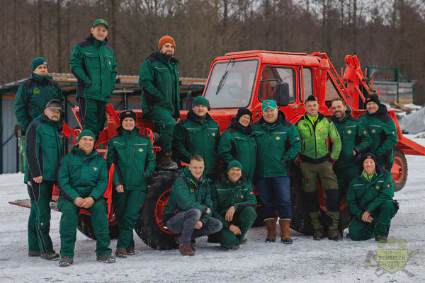 Teamfoto des Forstbetriebs Behrisch vor einem restaurierten roten Forsttraktor im Schnee