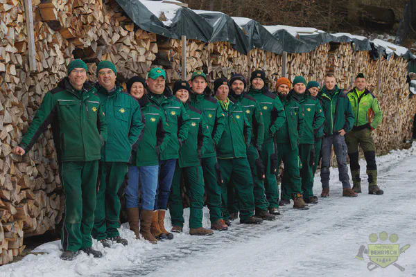 Das Team in Forstkleidung vor Holzstapeln im winterlichen Erzgebirge