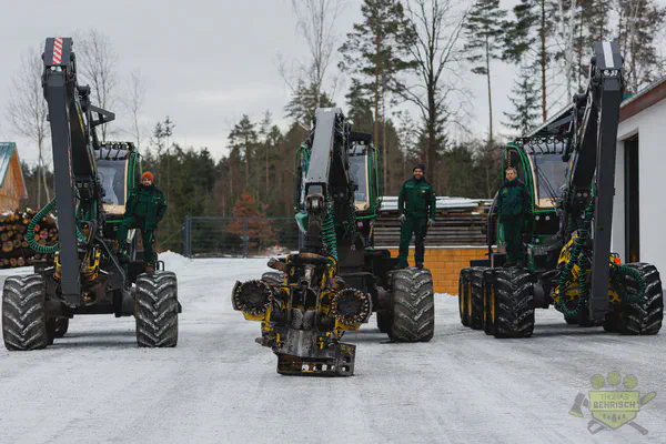 Drei Harvester-Fahrer vor ihren John Deere Harvestern mit Fällköpfen auf dem Betriebsgelände